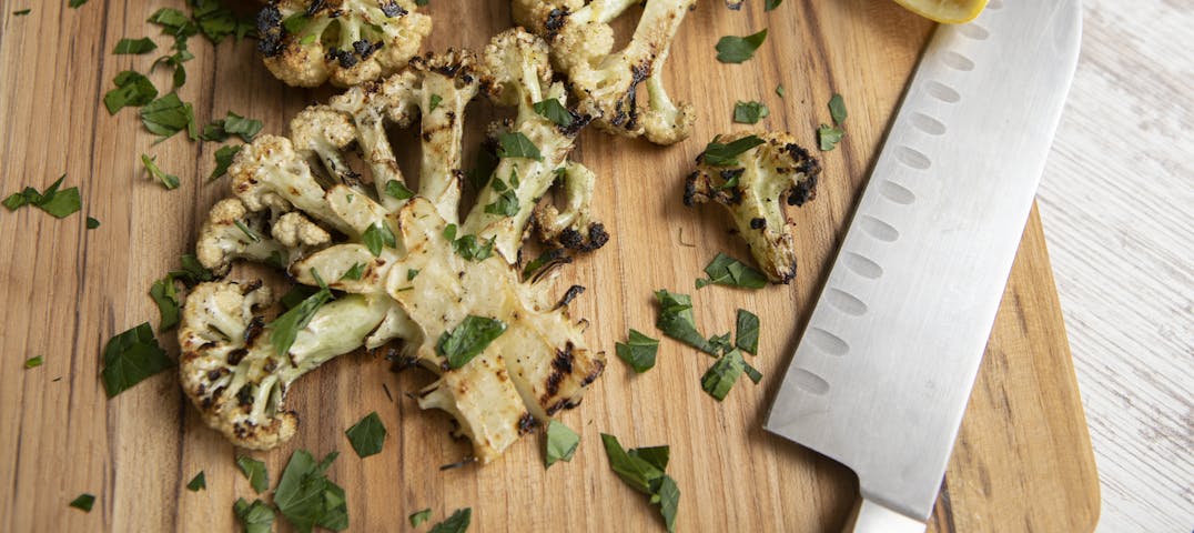 A cutting board with seasoned cauliflower and knife.