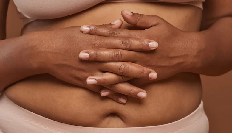 A woman holds her hands over her stomach.