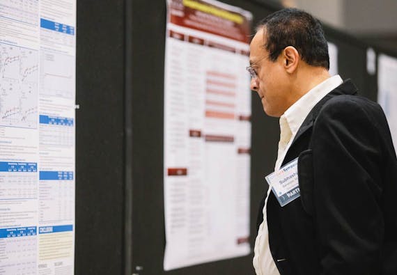 A male in a suit inspects a research poster at a training symposium. 