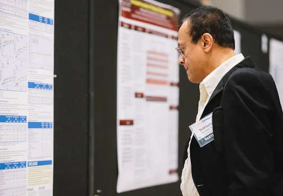 A male in a suit inspects a research poster at a training symposium.