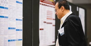 A male in a suit inspects a research poster at a training symposium. 