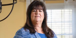 Jody Quinn, wearing a blue shirt and sweater, poses in a bright room.