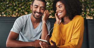 A man and a woman share headphones at a restaurant.