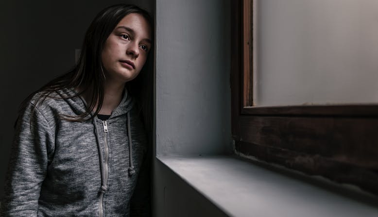 A teenage girl looks out the window looking sad.