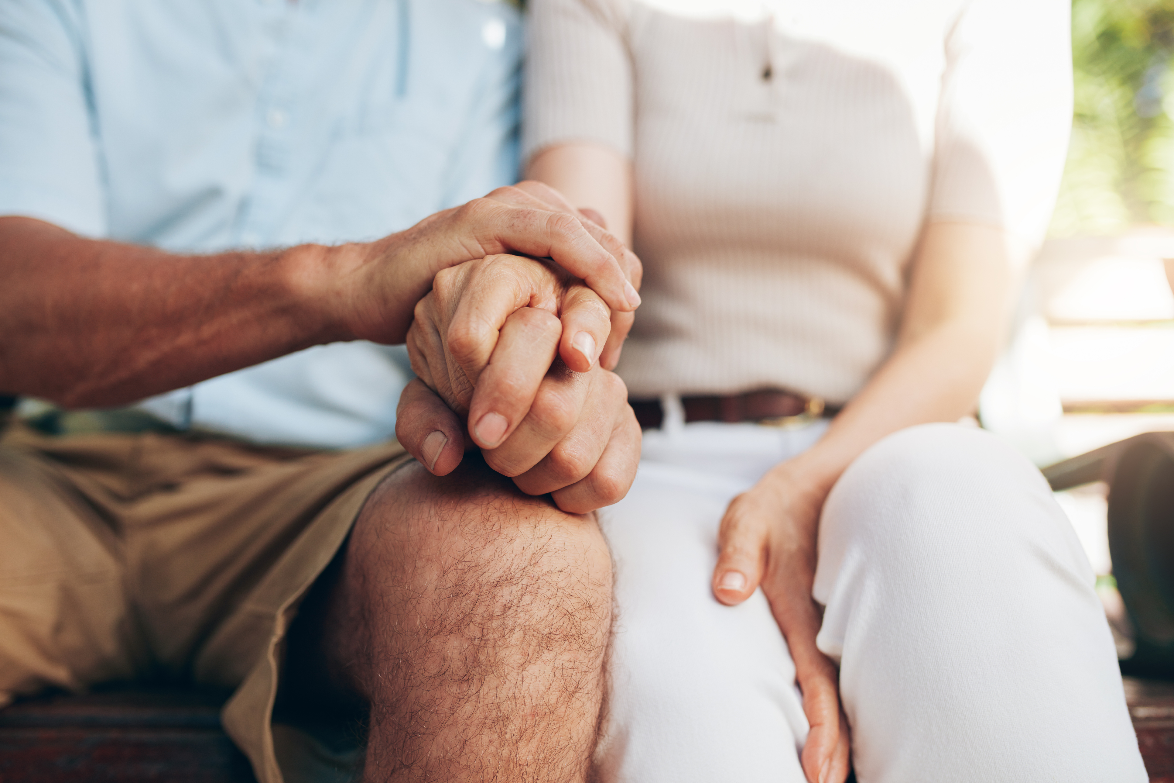 A couple sits on a bench holding hands.