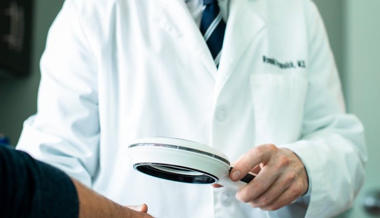 Dr. Prussick examines a patient's hands under a magnifying glass.