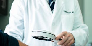 Dr. Prussick examines a patient's hands under a magnifying glass. 