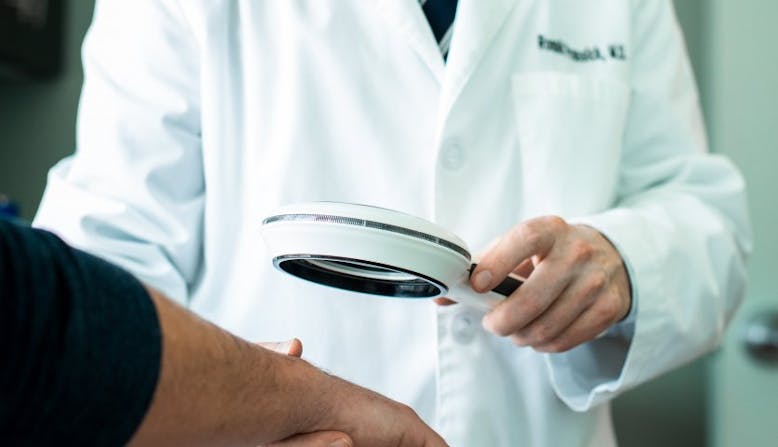 Dr. Prussick examines a patient's hands under a magnifying glass.