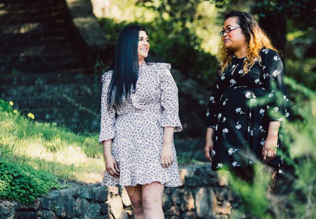 Two young women in a park walk on a pathway and converse.