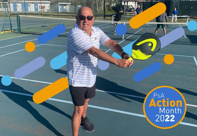 A man is posing on a tennis court with a racquet. The logo for PsA Action Month 2022 is overlaid.