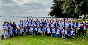 A large group of people wearing AnaptysBio branded shirts posing outside with trees and water in the background.