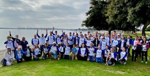 A large group of people wearing AnaptysBio branded shirts  posing outside with trees and water in the background.