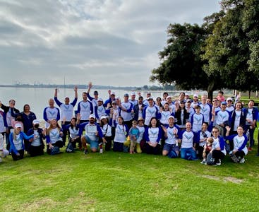 A large group of people wearing AnaptysBio branded shirts posing outside with trees and water in the background.