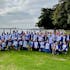 A large group of people wearing AnaptysBio branded shirts  posing outside with trees and water in the background.