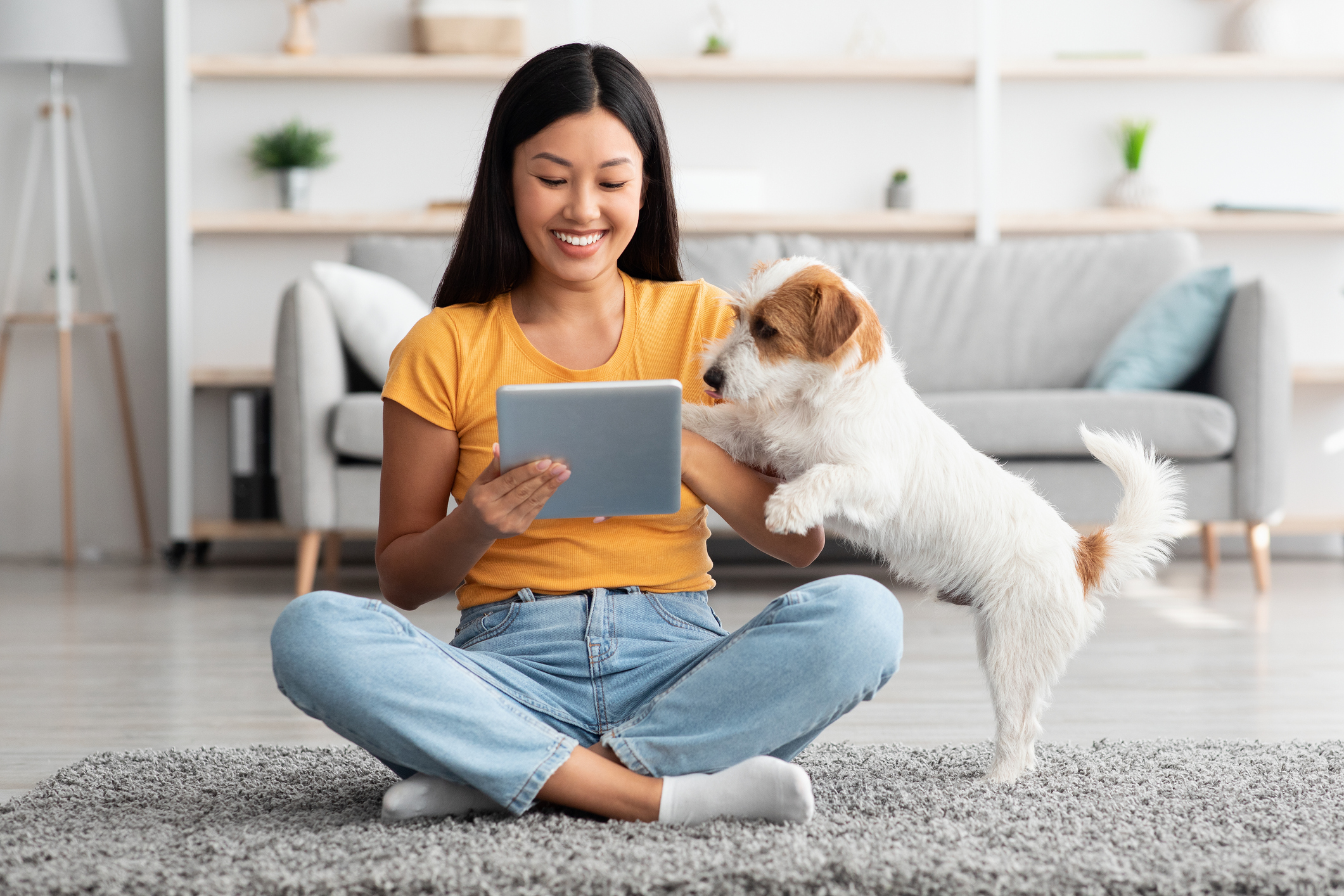 A woman sitting on the floor with her tablet and dog.