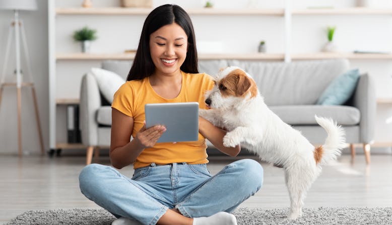 A woman sitting on the floor with her tablet and dog.