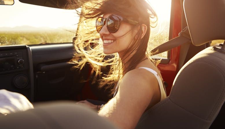 Young woman sits in the passenger seat of a car smiling.