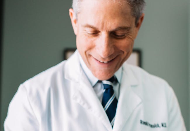 A male doctor inspects a hand under a magnifying glass and smiles.