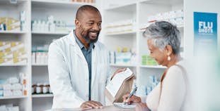 A pharmacist hands a prescription bag to a patient.