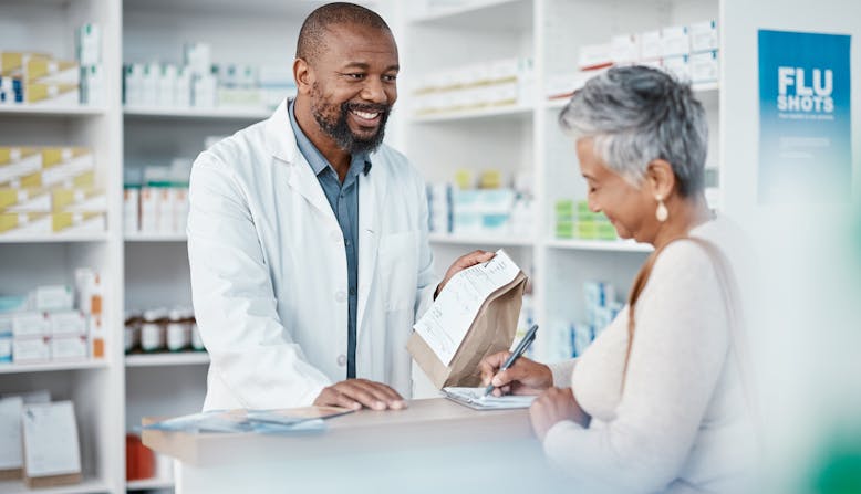 A pharmacist hands a prescription bag to a patient.