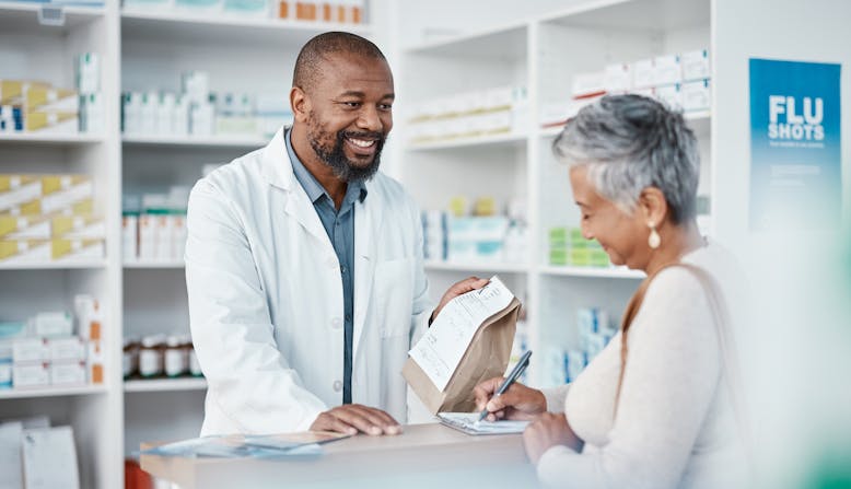 A pharmacist hands a prescription bag to a patient.