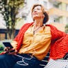 Woman sits on a bench listening to something on her phone.