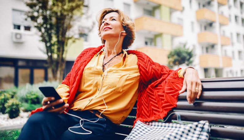Woman sits on a bench listening to something on her phone.