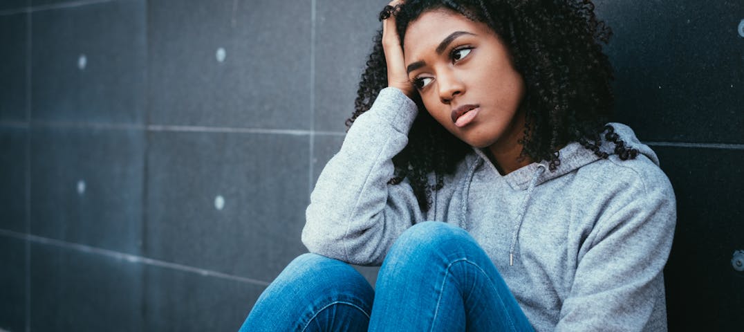 A woman sits by a wall looking off into the distance and thinking.