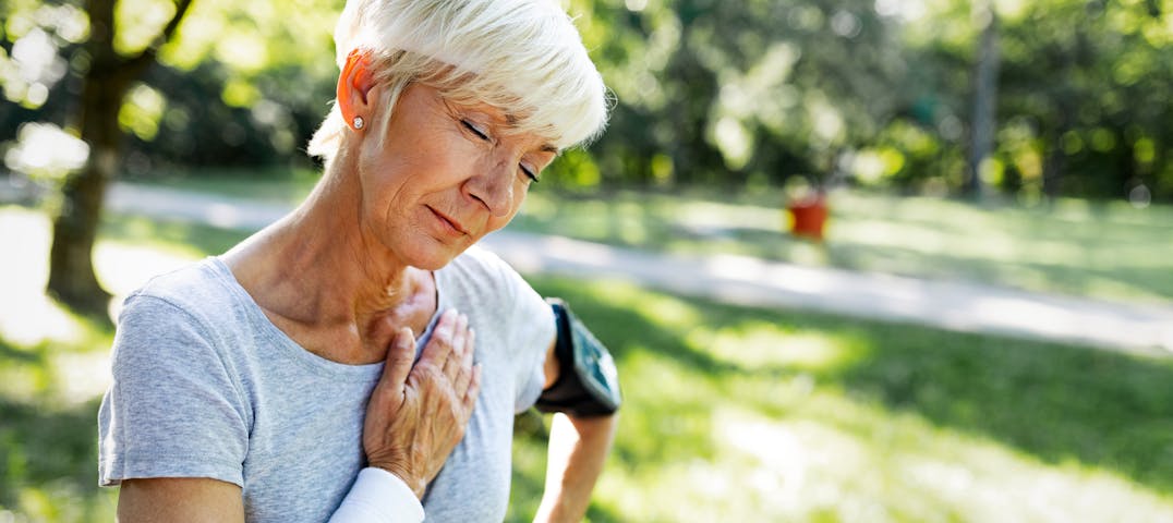 An older woman places her hand on her chest while working out.