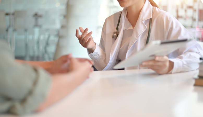 A woman doctor holds a clipboard and explains something to a patient.