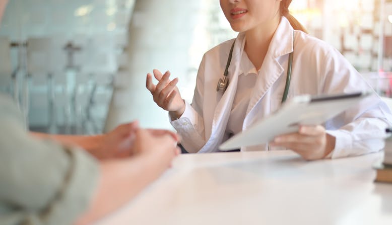 A woman doctor holds a clipboard and explains something to a patient.
