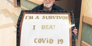 John Jones sits in a wheelchair and holds a sign celebrating his recovery from COVID-19.