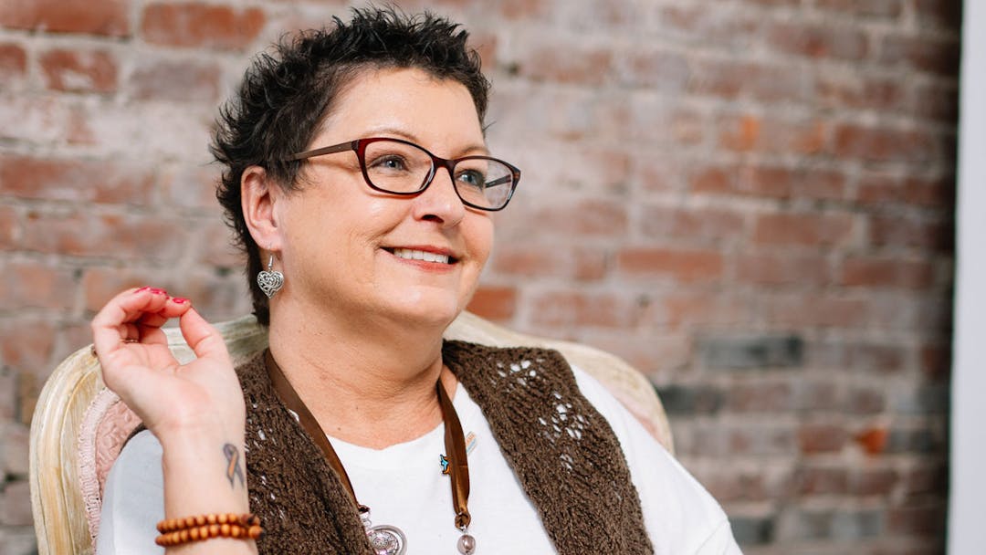A woman with psoriasis sitting in a chair and smiling.