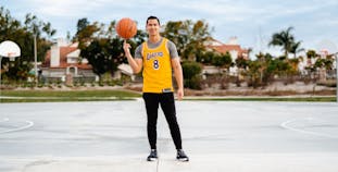 Christian Jacobe stands on a basketball court balancing a basketball on his finger and wearing a Lakers jersey.