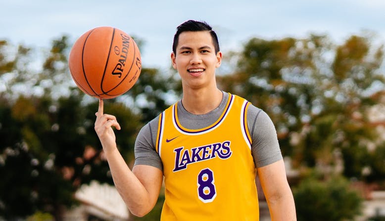 Christian Jacobe stands on a basketball court balancing a basketball on his finger and wearing a Lakers jersey.