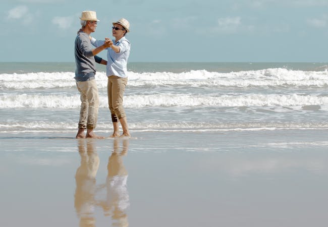 An elderly couple dances on the beach.