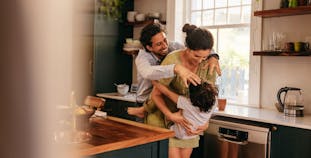 A mom and dad play with their young child in the kitchen.