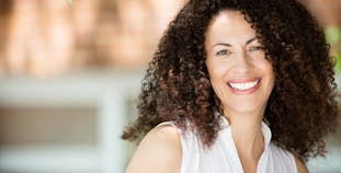 A lady with curly brown hair smiling outside. 