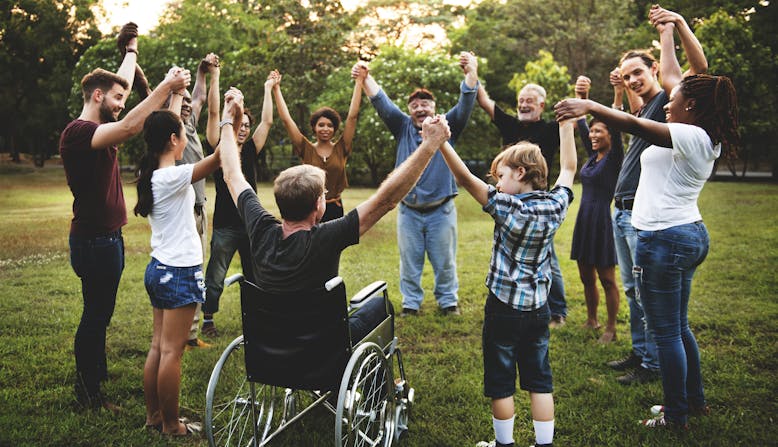 Group of diverse people, children and adults, holding hands in a circle at a park.