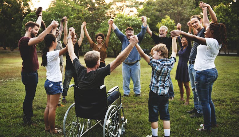 Group of diverse people, children and adults, holding hands in a circle at a park.