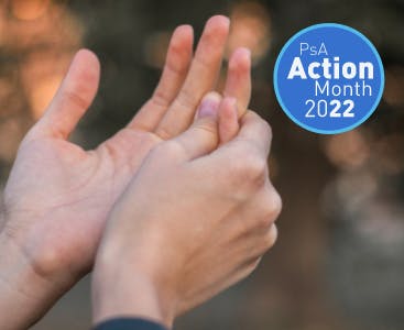One hand gripping another as if in pain. A graphic for PsA Action Month 2022 overlaid.