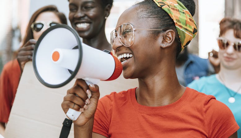 A young woman holding a megaphone and smiling at a group protest.
