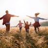 A family walk through a field together, with their arms out.
