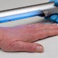 A hand with light skin and visible psoriasis on a surface with a gloved hand holding a phototherapy device above.