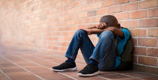 An upset child sitting outside at school.