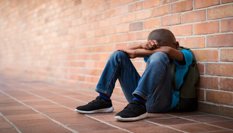 A boy sits outside of school after being bullied.