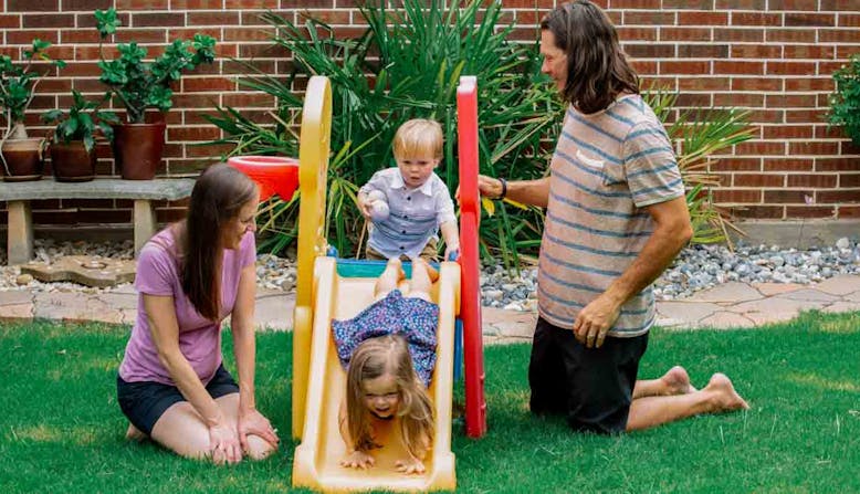 A family with two small children play outside on a playground.