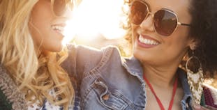 Two women wearing sunglasses and smiling outside.