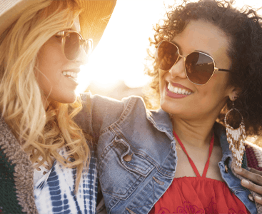 Two women wearing sunglasses and smiling outside.