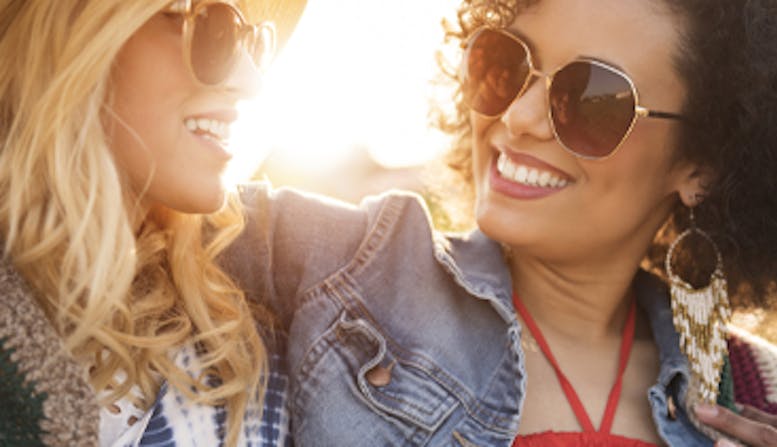 Two women wearing sunglasses and smiling outside.